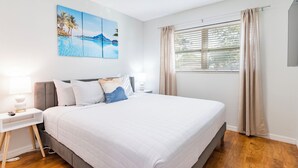 A bedroom with a bed, a nightstand, a lamp, a painting, and a window with curtains. - Heated Private Pool + Game Room | Family & Group Favorite | Beach Minutes Away (Largo)