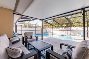 Ett takförsett utomhusområde med en pool, sittplatser och utsikt över trädgården.
