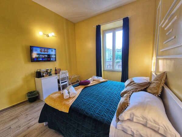 Una habitación de hotel con cama, escritorio, televisor y ventana con cortinas.