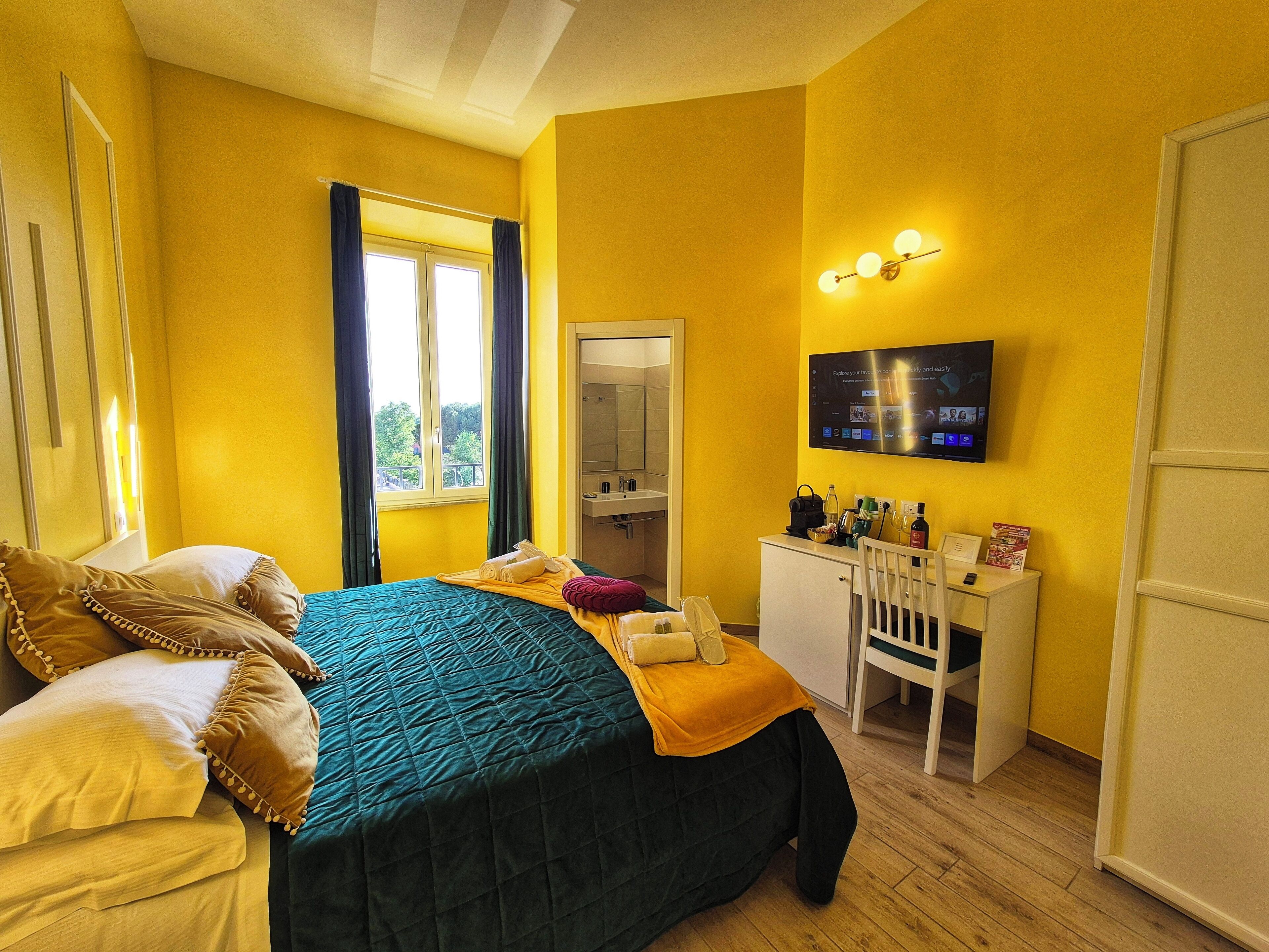 A hotel room with a bed, a desk, a mirror, a TV, and a window with curtains.