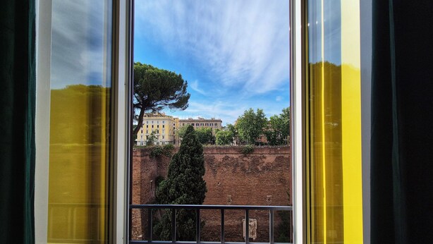 A window with a view of a building, a tree, and a brick wall. - RESIDENZE SERVENTI LONGHI (Rome)
