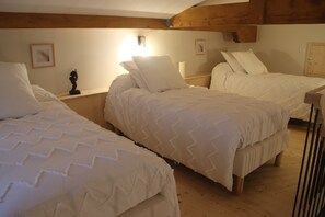 Una habitación con tres camas dispuestas en fila, vigas de madera en el techo y un estante con una estatua.