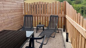 A wooden deck with two lounge chairs and a table, surrounded by a wooden fence, overlooking a green landscape. - Gîte Lucanna Apartment with terrace for 5 people (Unknown)