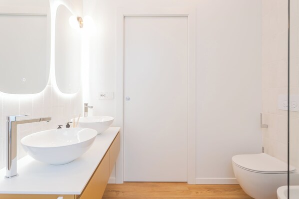 Un baño moderno con un lavamanos grande de color blanco, un espejo y un inodoro.