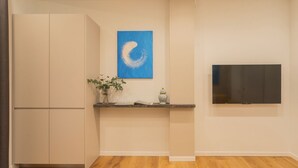 A modern kitchen with a built-in oven, a flat-screen TV mounted on the wall, and a wooden floor.