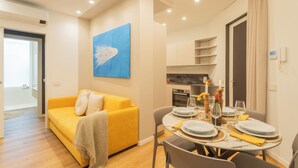 A modern living room with a yellow sofa, a dining table set for four, and a kitchen area in the background.