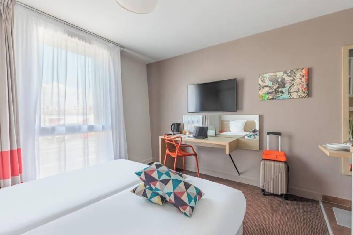 Een hotelkamer met een bed, een bureau, een stoel, een televisietoestel en een raam met gordijnen.