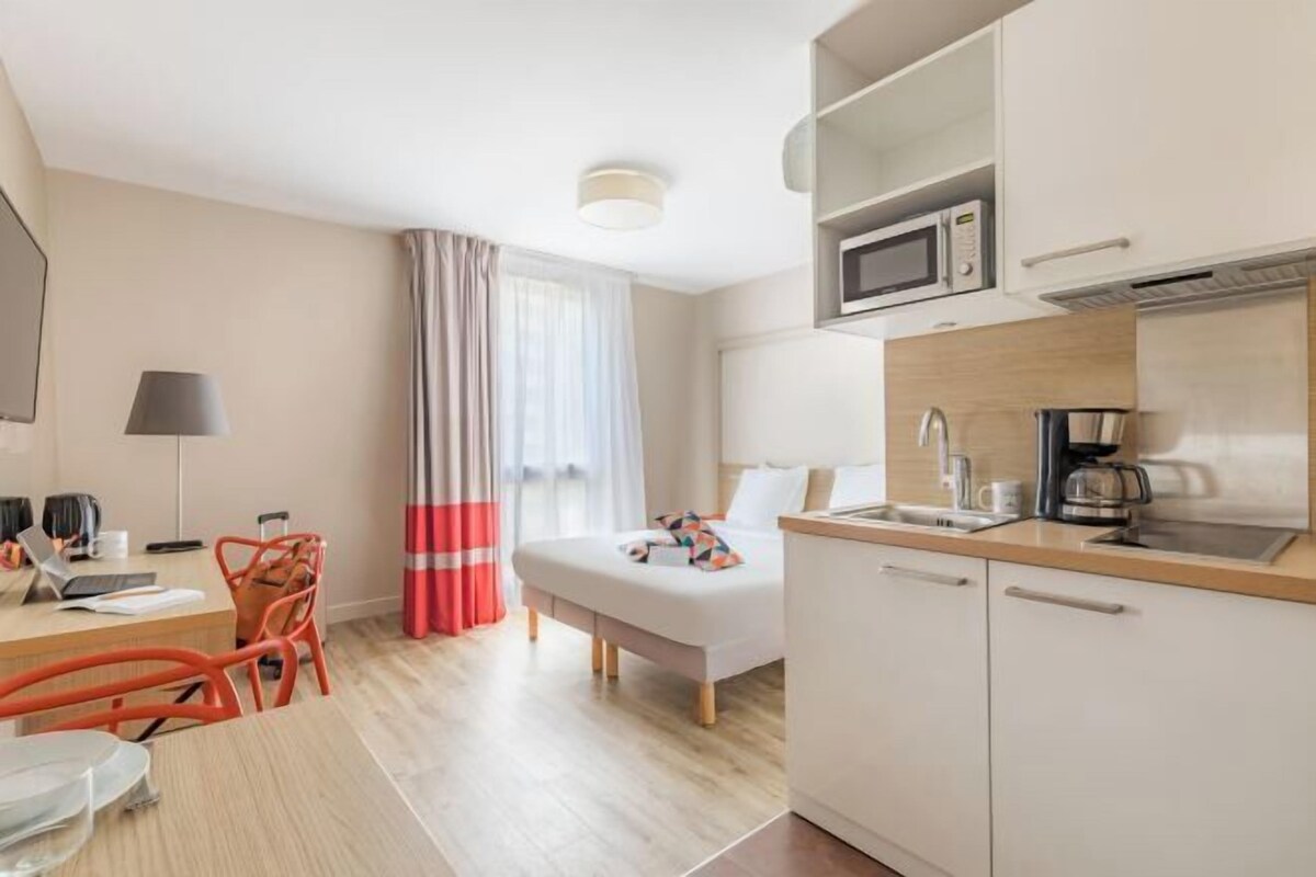 Hotelkamer met een bed, een bureau met een laptop, een stoel, een magnetron, een koffiezetapparaat en een wastafel.
