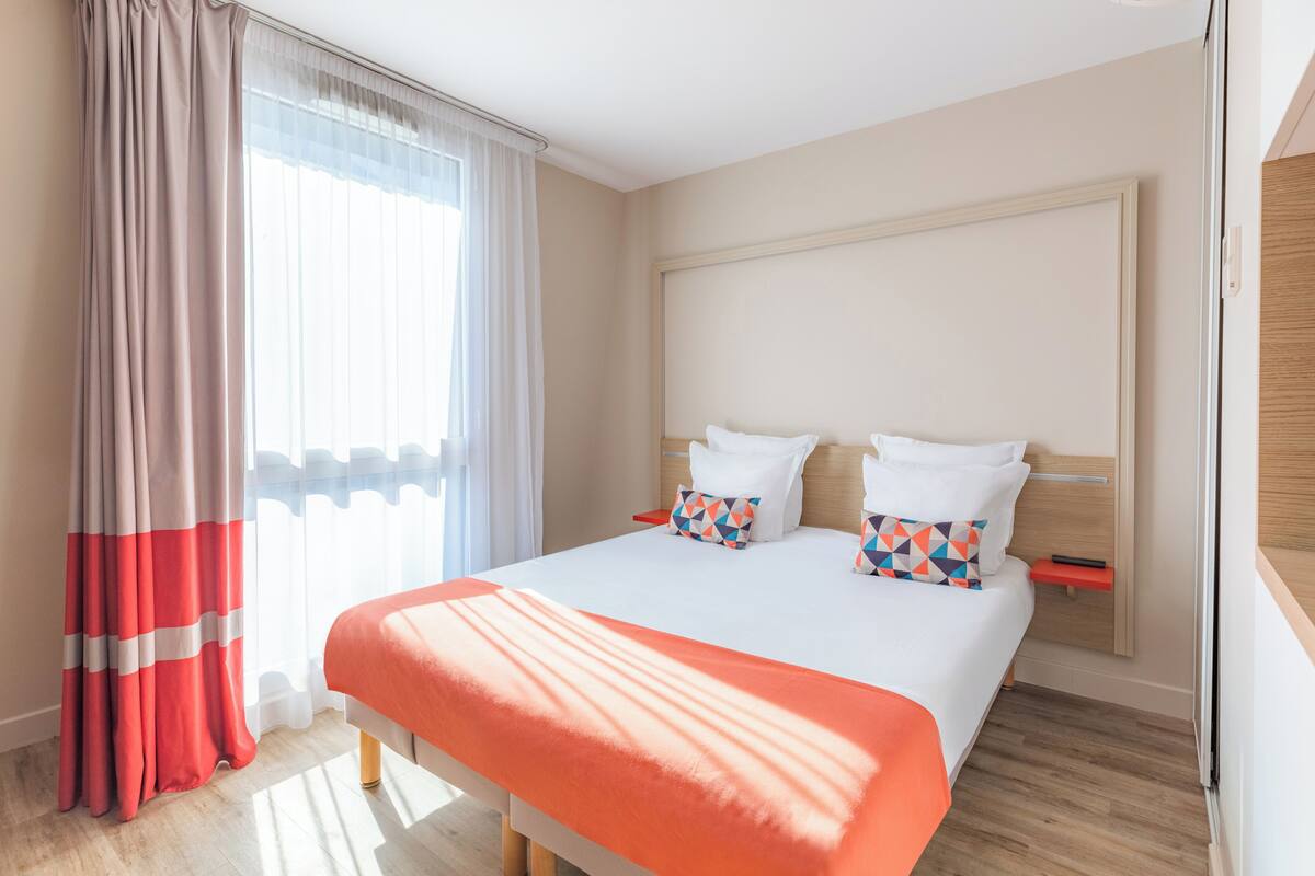 Een hotelkamer met een groot bed, een nachtkastje en een raam met gordijnen.