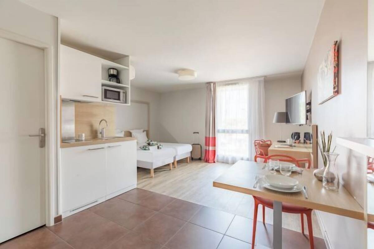Een compact hotelkamer met een kitchenette, een eethoek en een bed.