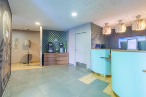 A reception area with a counter, a small table with a plant, and a wall with a geometric pattern.