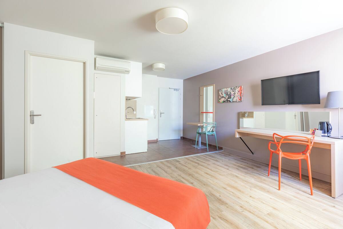 Een hotelkamer met een bed, een bureau met stoel, een televisie en een zichtbare badkamer op de achtergrond.