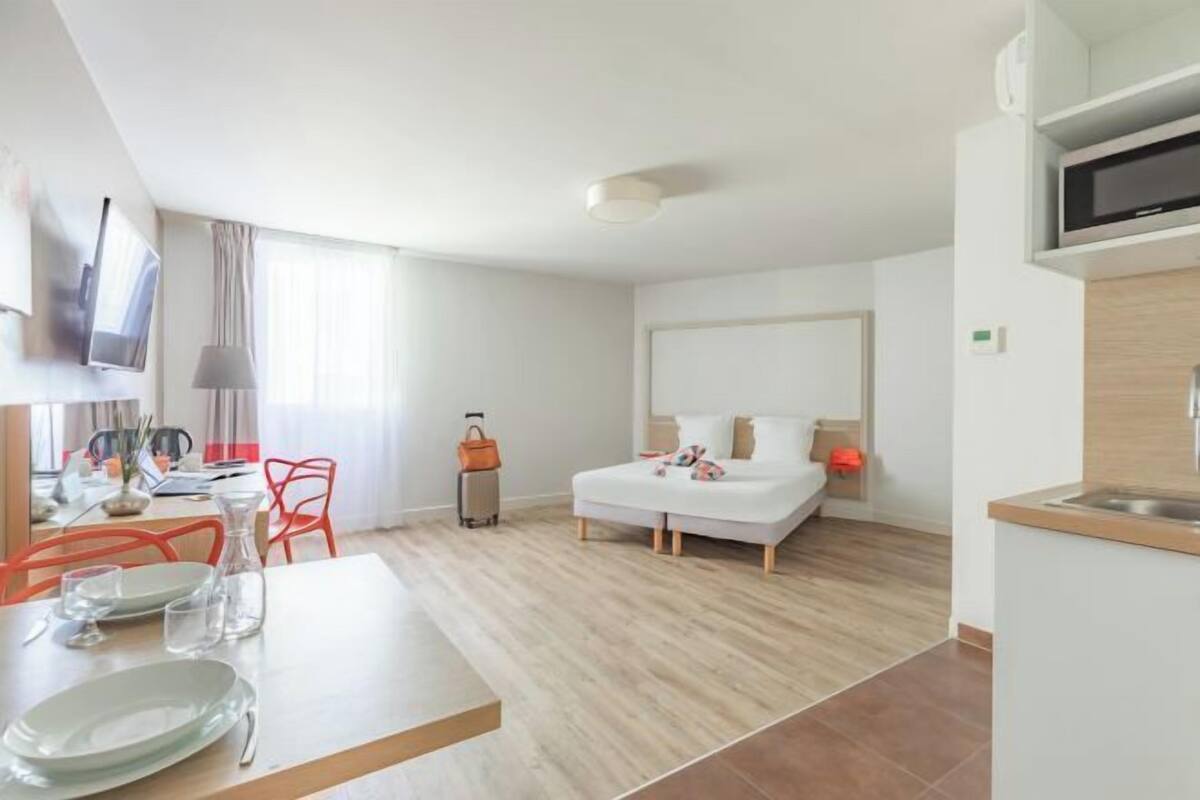 Hotelkamer met een bed, bureau, stoel, televisie, magnetron en een kleine keukenhoek.
