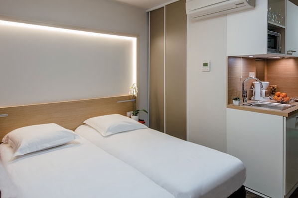 A hotel room with two beds, a bedside table with a plant, a small sink, and a microwave.