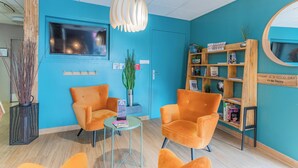 A reception area with two orange chairs, a small table, a bookshelf, and a television on the wall.