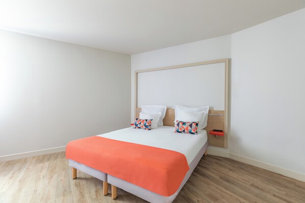 A neatly made bed with an orange bedspread, white pillows, and a wooden headboard.