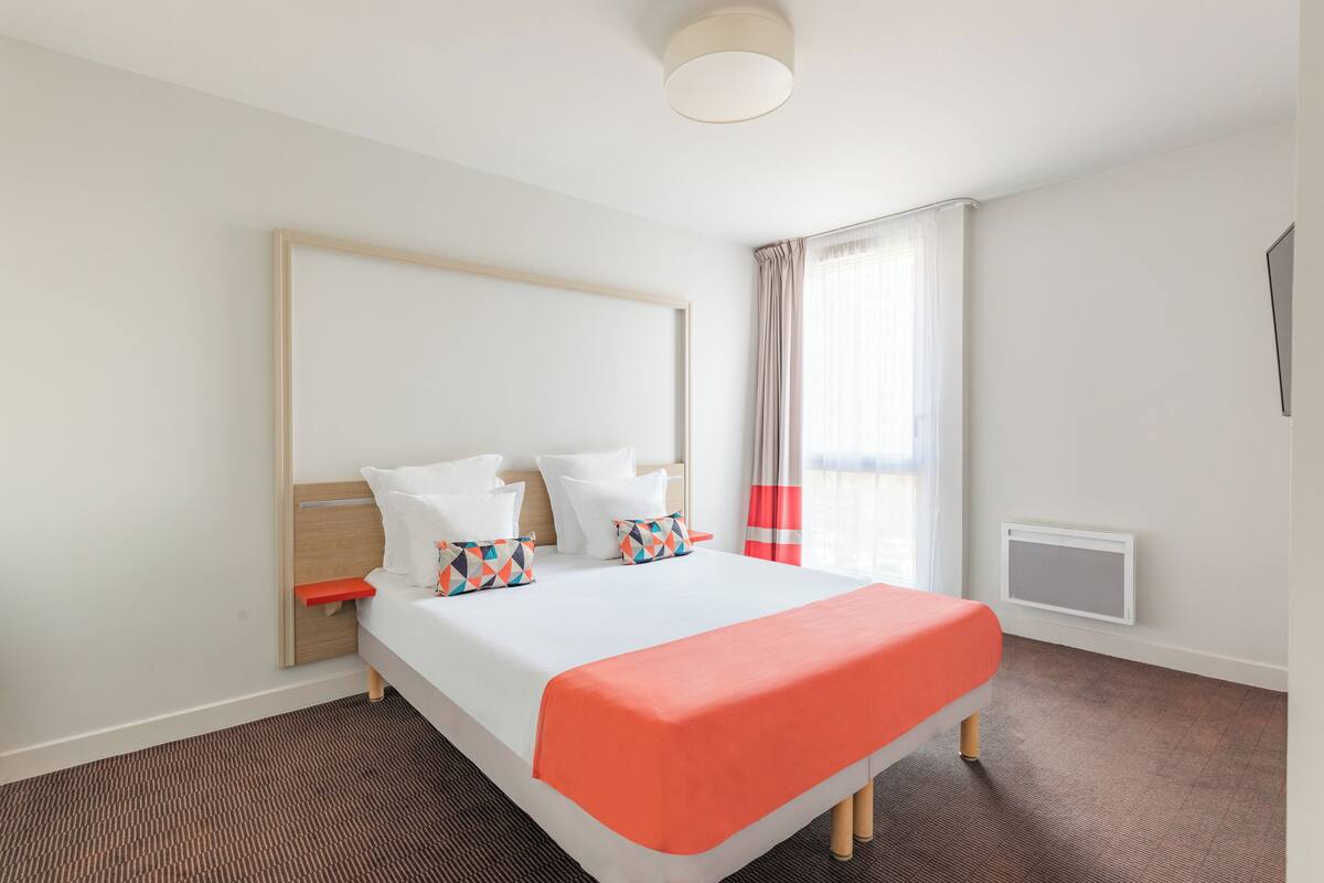 Een hotelkamer met een bed, nachtkastje, raam met gordijnen en een wandradiator.