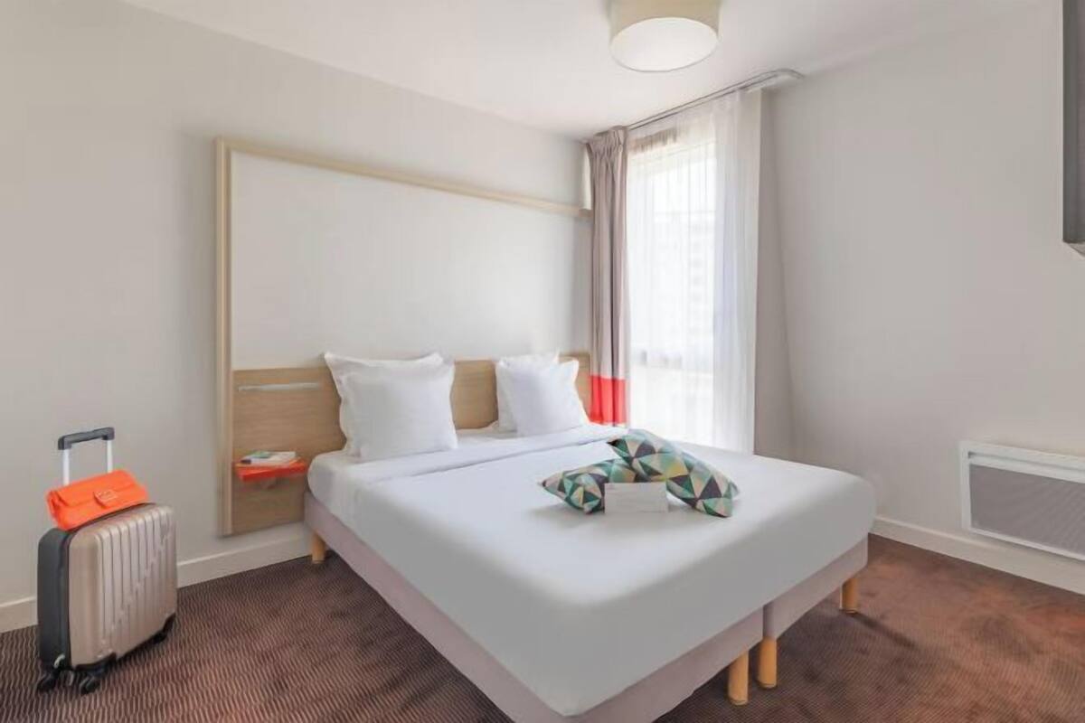 Een hotelkamer met een bed, een koffer en een raam met gordijnen.