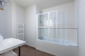 Een moderne badkamer met een douchecabine van glas, een witte wastafel en een handdoekrek.