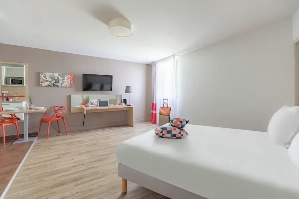 A hotel room with a bed, desk, chair, TV, and a window with curtains.