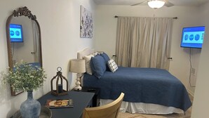 A bedroom with a bed, a desk, a chair, a mirror, a lamp, a vase with flowers, and a ceiling fan. - Charming 1-bedroom condo in welcoming Tallahassee with WiFi, AC (Tallahassee)