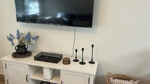A flat-screen TV mounted on a wall above a white console with a decorative vase, a chessboard, and a small table. - Charming 1-bedroom condo in welcoming Tallahassee with WiFi, AC (Tallahassee)