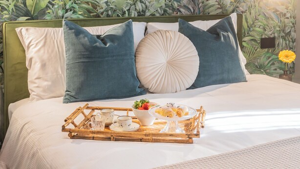 A neatly made bed with a tray of breakfast items, including pastries and a bowl of fruit, set against a backdrop of lush green foliage. - Rezia Apartments - Bellagio Suite (Como)
