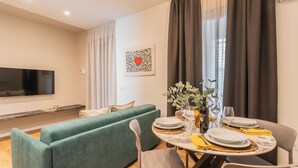 A modern living room with a green sofa, a dining table set with plates, glasses, and a bottle, and a flat-screen TV mounted on the wall. - Rezia Apartments - Bellagio Suite (Como)