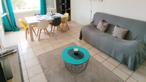 A living room with a grey sofa, a coffee table, a dining table with chairs, and a bookshelf.