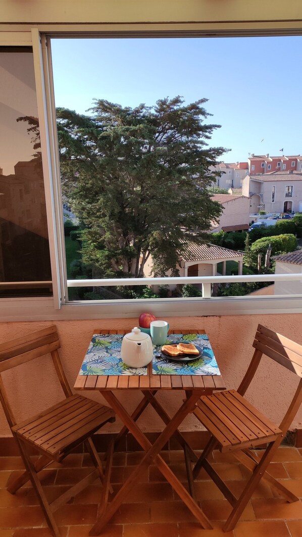 A balcony with a table set for two, featuring a teapot, a cup, and a plate with toast.