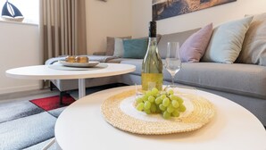 A modern living room with a round white table, a bottle of wine, and a glass of wine on a woven placemat. - Anchorage 3 - Terrace. Sauna. Dogs allowed. Barrier-free & close to the beach. (Kellenhusen)