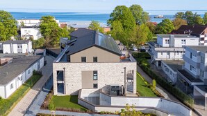 A modern residential building with a sloped roof, large windows, and a landscaped front yard. - Anchorage 3 - Terrace. Sauna. Dogs allowed. Barrier-free & close to the beach. (Kellenhusen)