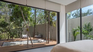 Ein modernes Schlafzimmer mit großem Fenster, einer Holzdielen Terrasse und Blick auf Bäume.