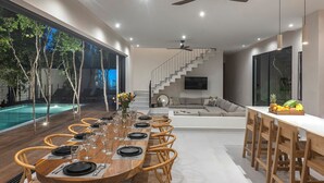 Ein modernes Esszimmer mit einem Holztisch, gedeckt für sechs Personen, einem Pool und einer Treppe, die in einen Wohnbereich mit einer Couch und einem Fernseher führt.
