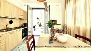 A modern kitchen with wooden cabinets, a black pot hanging on the wall, a dining table with a placemat, chairs, and a vase with flowers. - Beachfront house with garden and veranda (Nardò)