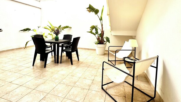 A small, bright room with a tiled floor, a table with chairs, two potted plants, and a white chair with a black frame. - Beachfront house with garden and veranda (Nardò)