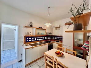 Une cuisine compacte avec un coin repas, dotée d’un plan de travail carrelé, de meubles en bois et d’un panier de fruits posé sur la table.