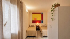 Ein Hotelzimmer mit zwei Betten, einem kleinen Tisch, einem Wandbild und einer Pflanze.