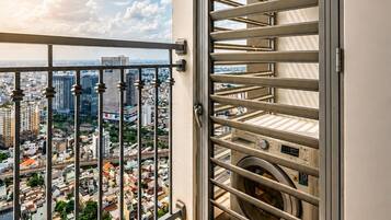 Un balcón con barandilla de metal, vistas de la ciudad y un lavadero con cestas de ropa apiladas.