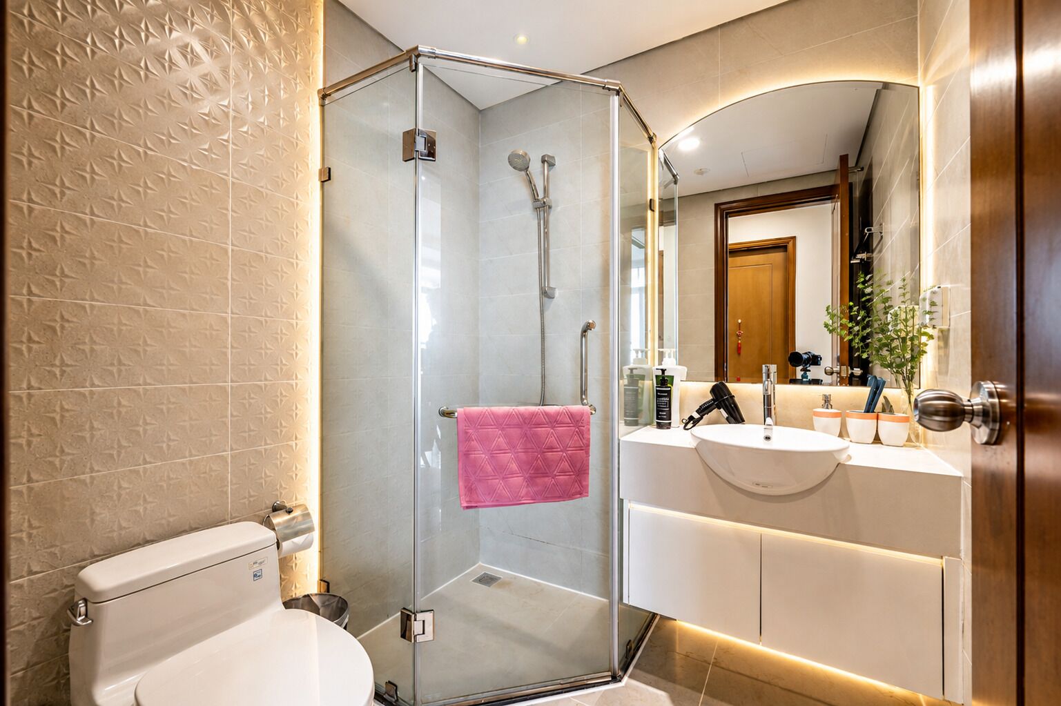 A modern bathroom with a glass-enclosed shower, a white toilet, and a vanity with a mirror.