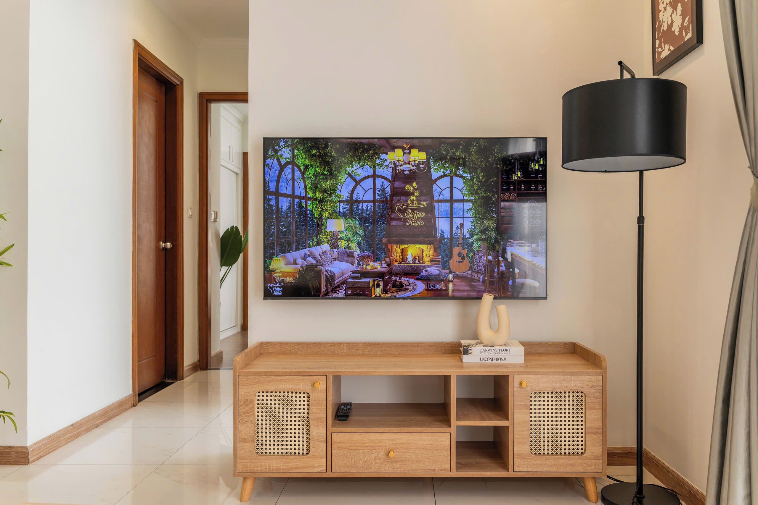 Un salon avec un téléviseur à écran plat fixé au mur, un meuble télé en bois avec une télécommande et une lampe sur pied.