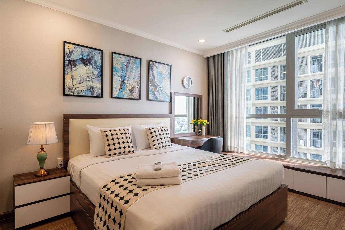 Une chambre d’hôtel avec un grand lit, une table de chevet avec une lampe, un bureau avec une chaise et une fenêtre donnant sur la ville.