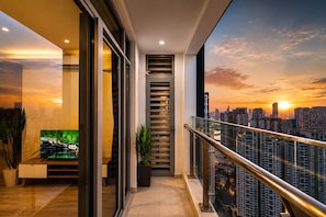 Un apartamento moderno con balcón, televisor y vista a la ciudad al atardecer.