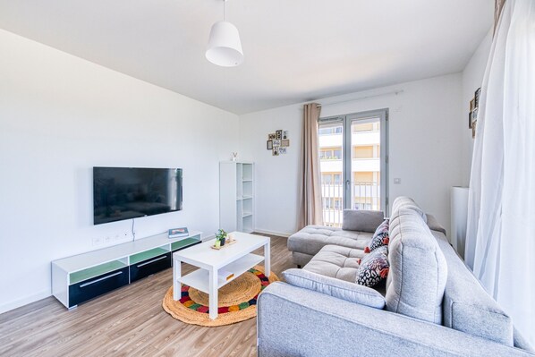 Un salon moderne avec un téléviseur à écran plat, un canapé gris, une table basse blanche et un plancher en bois.