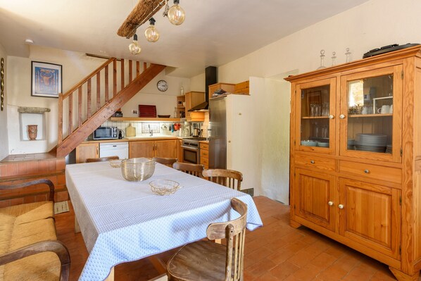 A kitchen with a dining table, chairs, a wooden cabinet, and a staircase.