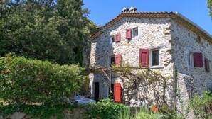 A stone building with red shutters, surrounded by greenery.