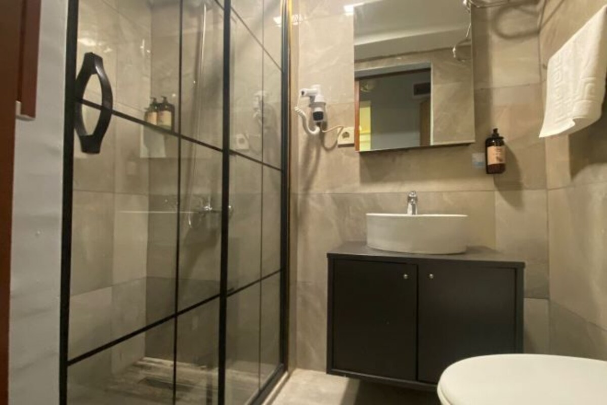 Un baño moderno con cabina de ducha de vidrio, tocador oscuro con lavamanos y espejo sobre el tocador.