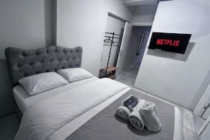 A modern hotel room with a large bed, a flat-screen TV, and a walk-in closet.
