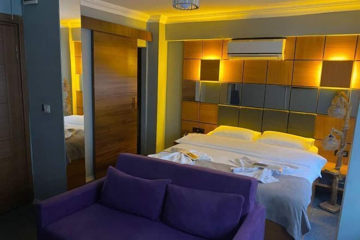 A hotel room with a bed, a purple sofa, and a wooden headboard with illuminated panels.
