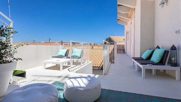A rooftop terrace with white furniture, a potted plant, and a view of the cityscape. - Darsena Sunset Apartment II by Wonderful Italy (Syracuse)